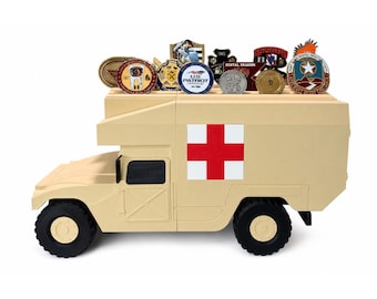 May include: A tan-colored military ambulance vehicle model featuring a red cross emblem on the side. The roof of the vehicle is slotted to hold a collection of various circular and shield-shaped commemorative challenge coins in different colors.
