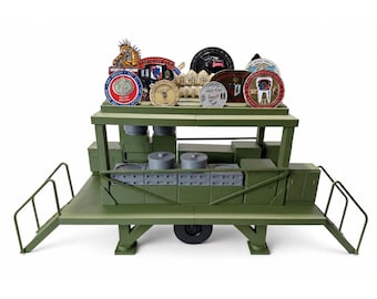 May include: An olive green military-style display stand featuring a two-tier structure with side railings and a central wheel. The top tier holds a collection of various circular and shaped metal challenge coins with colorful emblems and text.