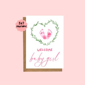May include: A 5x7 printable baby girl welcome card. The card features pink baby footprints inside a green leafy heart. The word "WELCOME" is above the words "baby girl" in pink script. The card is on a brown cardstock.