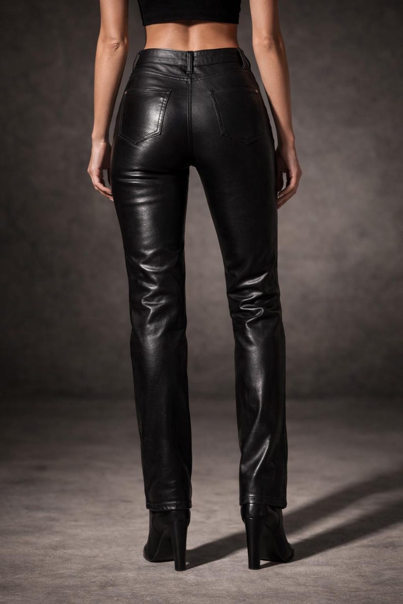 May include: Black leather pants with a high waist and a straight leg. The pants have a classic five-pocket design and are worn with black heeled boots. The leather has a slight sheen.