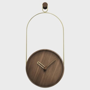 Puede incluir: Un reloj de pared moderno con una esfera redonda de madera oscura y manecillas doradas. El reloj está suspendido por un marco de metal dorado y una clavija de madera. La esfera tiene aproximadamente 20 cm de diámetro.