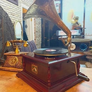 May include: A classic gramophone featuring a decorative brass horn and a dark wood cabinet. A vinyl record is placed on the turntable. The gramophone is on a wooden surface, with a vintage telephone visible.
