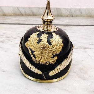 May include: A white ceramic mug with a black handle and the text "But First, Coffee" in a bold, black font. The mug is set against a blurred background, suggesting a cozy setting.