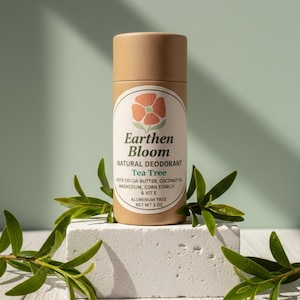 May include: A cylindrical, brown paper tube of Earthen Bloom Natural Deodorant, Tea Tree scent, with a floral logo. The label lists ingredients and says "Aluminum Free, Net Wt 3 oz." The deodorant sits on a white block, with green leaves.