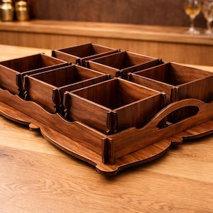 Pode incluir: Uma bandeja de madeira com seis compartimentos quadrados. A bandeja e os compartimentos são feitos de madeira marrom escura. A bandeja tem uma borda decorativa ondulada e um recorte de alça. A bandeja está em uma mesa de madeira.