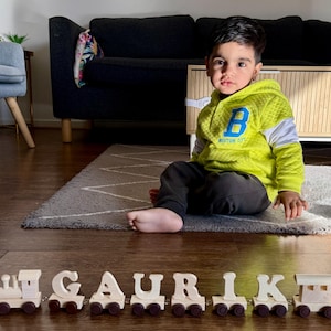 May include: A wooden toy train set consisting of a locomotive, a caboose, and individual train cars carrying the letters G, A, U, R, I, K, and E, each featuring small dark brown wheels and a light natural wood finish for the letter blocks.
