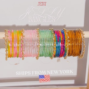 May include: A selection of vibrant jelly bangles in pink, green, yellow, orange, blue, and gold. The bangles are presented on a wooden dowel, with the words "JELLY BANGLES" displayed above.