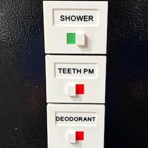 May include: A vertical stack of five white rectangular plastic task trackers with sliding switches. Each tracker features a black printed label: WORKOUT, SHOWER, TEETH PM, DEODORANT, and MELATONIN. The switches reveal green or red color indicators.