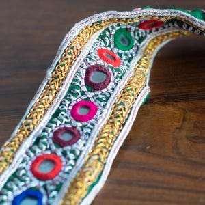 Puede incluir: Borde de tela verde con bordado de hilo dorado y plateado y adornos redondos de espejo. El borde presenta acentos rojos, azules y marrones.