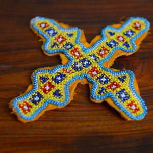 Peut inclure: Une croix en tissu jaune, bleue et rouge, ornée de perles colorées et d'un motif géométrique.