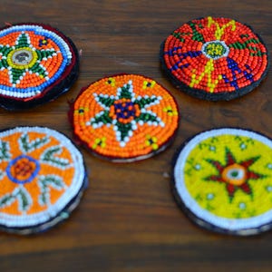 May include: Five round beaded ornaments with colourful geometric patterns. Each ornament features a central star shape with a variety of colours, including orange, yellow, red, green, and blue.