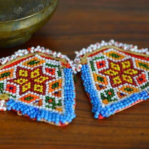 Op de afbeelding: Een paar kleurrijke kralen oorbellen met een geometrisch patroon. De oorbellen zijn hartvormig en hebben een blauwe, witte, rode, gele en groene kleurstelling.