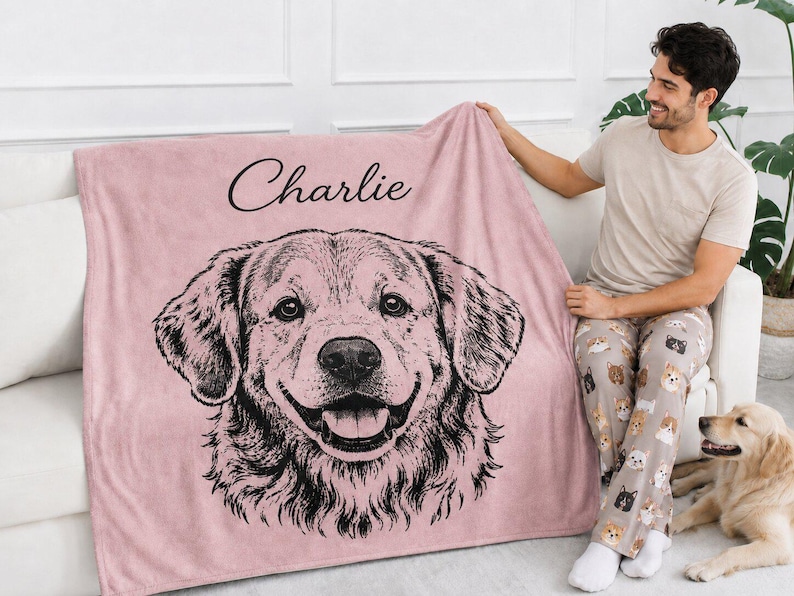 Puede incluir: Una manta de forro polar de color rosa empolvado suave con una ilustraci&oacute;n de l&iacute;neas negras de la cara de un golden retriever en el centro. El nombre Charlie est&aacute; impreso en cursiva negra sobre la ilustraci&oacute;n del perro.