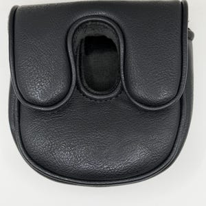 May include: A black putter headcover with a textured, leather-like finish. The cover features a rounded, U-shaped design with a central opening and a flap closure, providing a protective shell for a golf club head with a sleek, solid black appearance.