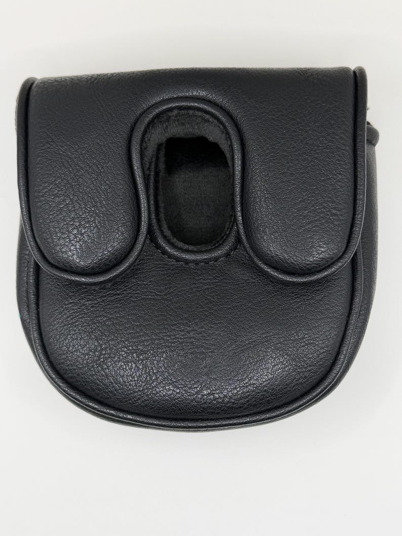 May include: A black putter headcover with a textured, leather-like finish. The cover features a rounded, U-shaped design with a central opening and a flap closure, providing a protective shell for a golf club head with a sleek, solid black appearance.