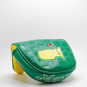 Könnte beinhalten: Grüne Golfschlägerhaube mit dem Wort "Masters" in weißer Schrift. Die Haube zeigt eine Karte des Augusta National Golf Club in Gelb und Grün mit einer roten Flagge. Die Innenseite der Haube ist gelb.