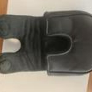 May include: A black leather golf club headcover featuring a U-shaped cutout design on one end and a rounded, padded top section. The material displays a smooth texture with visible stitching along the edges and a slightly gathered, flexible middle.