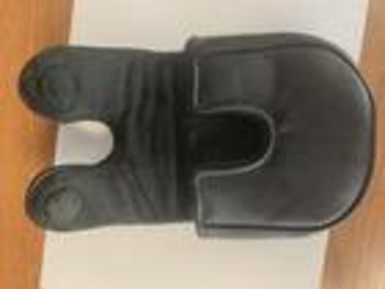 May include: A black leather golf club headcover featuring a U-shaped cutout design on one end and a rounded, padded top section. The material displays a smooth texture with visible stitching along the edges and a slightly gathered, flexible middle.