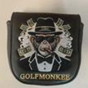 May include: A black golf putter headcover featuring an embroidered graphic of a monkey wearing a tuxedo, fedora, and sunglasses while smoking a cigar. The design includes white smoke accents and the text GOLFMONKEE printed in gold at the bottom.