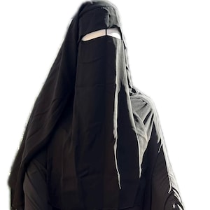 Może przedstawiać: Pokazano czarny nikab, czyli zasłonę na całą twarz noszoną przez niektóre muzułmanki. Ubranie zakrywa całe ciało, z otworem na oczy. Tkanina wydaje się być ciemnym, nieprzezroczystym materiałem. Nikab to tradycyjny strój.