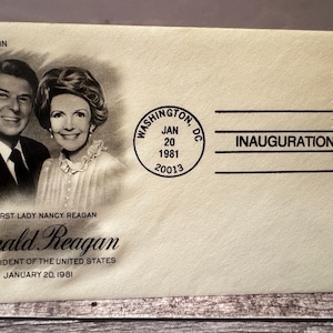May include: Cream-colored envelope commemorating Ronald Reagan's inauguration. Features a black and white portrait of Ronald and Nancy Reagan, with text including "INAUGURATION DAY" and "40th President of the United States". Includes a US postage stamp.