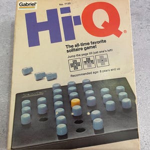 Peut inclure: Une boîte de jeu de solitaire Gabriel Hi-Q avec le texte Hi-Q, The all-time favorite solitaire game!, Jump the pegs till just one's left!, et Recommended age: 8 years and up. La boîte montre un plateau de jeu noir avec des pions bleus et jaunes.