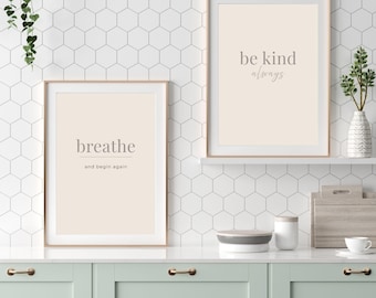 May include: Two framed art prints with motivational quotes. One print says "breathe and begin again" and the other says "be kind always". The prints have a neutral colour palette and are displayed in a kitchen setting.