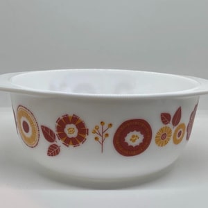 May include: White ceramic bowl with a floral pattern in shades of orange and yellow. The bowl has a wide rim and a rounded shape. The floral design includes stylized flowers and leaves, adding a vintage touch to the kitchenware.