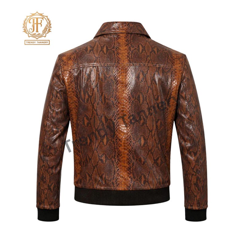 May include: A brown jacket featuring a snakeskin pattern throughout the exterior. The garment includes a pointed collar, long sleeves with black ribbed cuffs, and a black ribbed hem at the waist. The Trendy Tannery logo is visible in the top left corner.