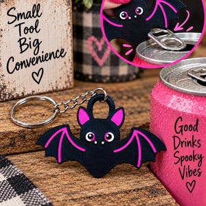 May include: A black bat-shaped keychain with bright pink accents on the ears and wings. The bat features white eyes and serves as a can tab opener. The text on the image includes 'Small Tool Big Convenience', 'Good Drinks Spooky Vibes', and 'Slides on the tab'.