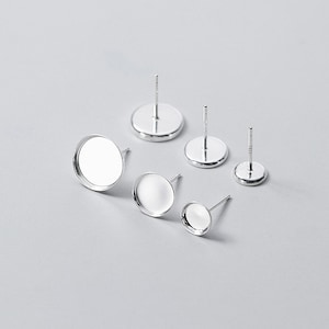 Könnte beinhalten: Satz mit fünf silberfarbenen Ohrringrohlingen mit runden Zargen. Die Zargen sind in verschiedenen Größen und zum Befestigen von Cabochons gedacht.