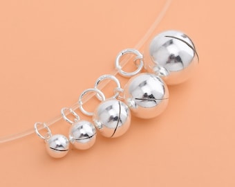 May include: A set of six silver jingle bells of varying sizes, each with a small loop for attaching to a project. The bells are arranged in a line from largest to smallest.