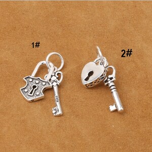 May include: Two silver charm pendants, one with a padlock and key, the other with a heart-shaped padlock and key. Both charms are detailed with intricate designs.