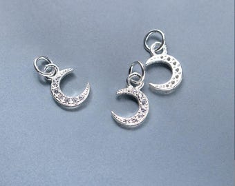 May include: Three silver-colored crescent moon charms with small loops for hanging. Each charm is detailed with small, clear stones along the curve of the moon. The charms are displayed on a light gray background.