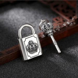 May include: A silver padlock with a crown design and a matching silver key with a crown design.