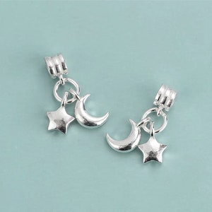 May include: Two silver charm pendants featuring a crescent moon and a star. Each charm is attached to a silver ring.
