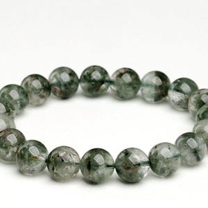 Op de afbeelding: Een armband met ronde, doorschijnende kralen met groene en bruine insluitsels. De kralen zijn geregen tot een cirkelvormige armband. De afbeelding toont de armband tegen een witte achtergrond, waardoor de natuurlijke kleuren en texturen van de stenen worden benadrukt.