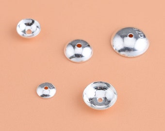 May include: Five silver-toned metal bead caps of varying sizes. The caps are round and have a small hole in the center.