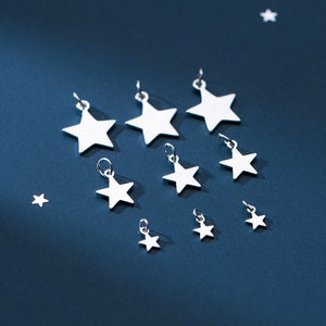 May include: A collection of silver star charms of varying sizes, arranged on a blue background. The charms are all in the shape of a five-pointed star and have a shiny, metallic finish.
