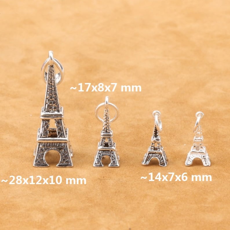 May include: Four silver Eiffel Tower charms of varying sizes. The largest charm measures approximately 28x12x10 mm, the next largest measures approximately 17x8x7 mm, and the two smallest charms measure approximately 14x7x6 mm.