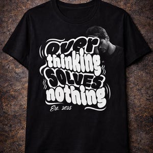 Puede incluir: Camiseta negra con el texto blanco "Overthinking Solves Nothing" en una fuente audaz y estilizada. La camiseta incluye el texto "Est. 2025" y una imagen en escala de grises de una persona. Una camiseta casual.