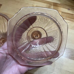 Pode incluir: Um prato de vidro prensado rosa com uma borda octogonal e uma base central de pedestal. A superf&iacute;cie do vidro &eacute; decorada com padr&otilde;es florais em relevo e linhas radiantes que se estendem do centro em dire&ccedil;&atilde;o &agrave;s bordas festonadas.