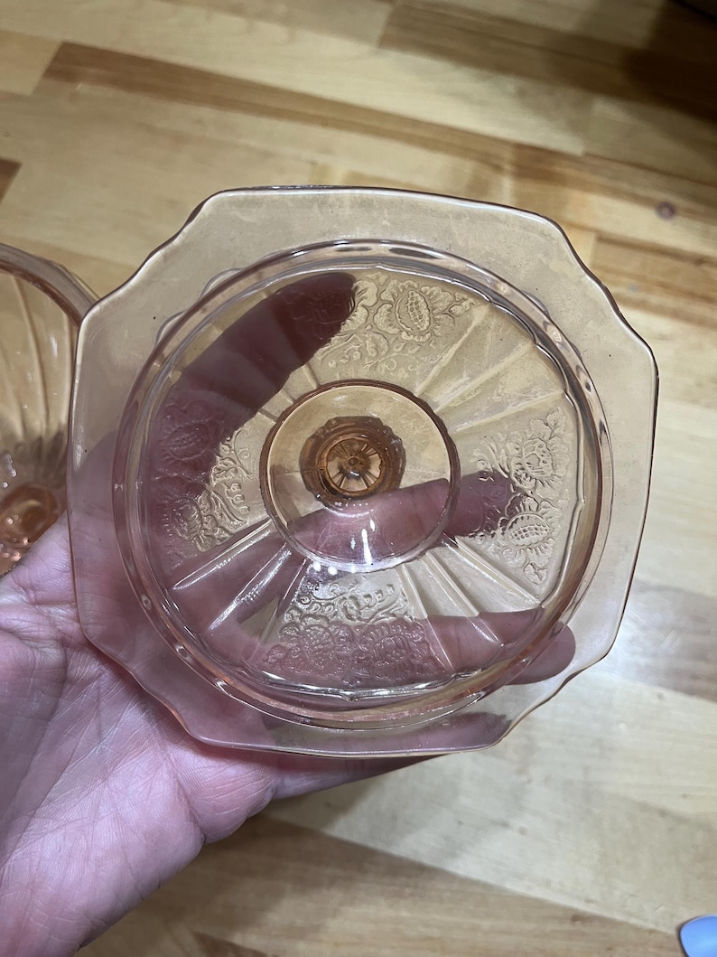 Pode incluir: Um prato de vidro prensado rosa com uma borda octogonal e uma base central de pedestal. A superf&iacute;cie do vidro &eacute; decorada com padr&otilde;es florais em relevo e linhas radiantes que se estendem do centro em dire&ccedil;&atilde;o &agrave;s bordas festonadas.