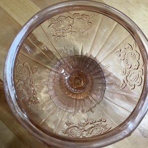 Pode incluir: Uma ta&ccedil;a de vidro rosa transl&uacute;cido com um padr&atilde;o floral em relevo nas paredes interiores. A ta&ccedil;a tem uma base circular e nervuras verticais que se estendem do centro at&eacute; &agrave; borda, criando um aspeto texturado e decorativo no objeto.