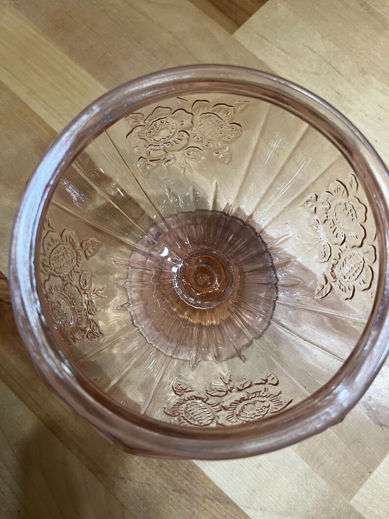 Pode incluir: Uma ta&ccedil;a de vidro rosa transl&uacute;cido com um padr&atilde;o floral em relevo nas paredes interiores. A ta&ccedil;a tem uma base circular e nervuras verticais que se estendem do centro at&eacute; &agrave; borda, criando um aspeto texturado e decorativo no objeto.