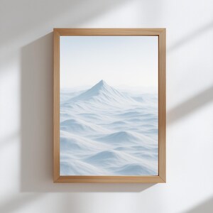 Könnte beinhalten: Ein gerahmter Druck mit einer schneebedeckten Berglandschaft. Das Kunstwerk zeigt einen zentralen Gipfel, umgeben von wellenförmigen, schneebedeckten Hügeln, unter einem blassblauen Himmel. Der Rahmen besteht aus hellem Holz und verleiht einen natürlichen Touch.