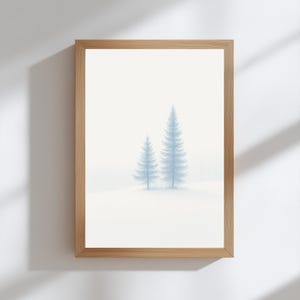 Könnte beinhalten: Ein gerahmter Druck mit einer ruhigen Winterlandschaft. Zwei hellblaue Tannen stehen in einem schneebedeckten Feld vor einem weichen, weißen Hintergrund. Das Kunstwerk ist in einem Naturholzrahmen eingefasst und schafft eine minimalistische Ästhetik.