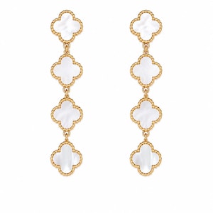 Peut inclure: Une paire de boucles d'oreilles pendantes dorées avec quatre pendentifs blancs en forme de trèfle. Les boucles d'oreilles ont une bordure dorée texturée et sont suspendues par de fines chaînes dorées. Le fond est blanc.