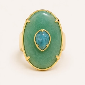 May include: A gold ring featuring a large oval green stone set in a polished gold frame with four prongs. Centered on the green stone is a smaller, teardrop-shaped blue stone held by four prongs, creating a layered, multi-stone design.