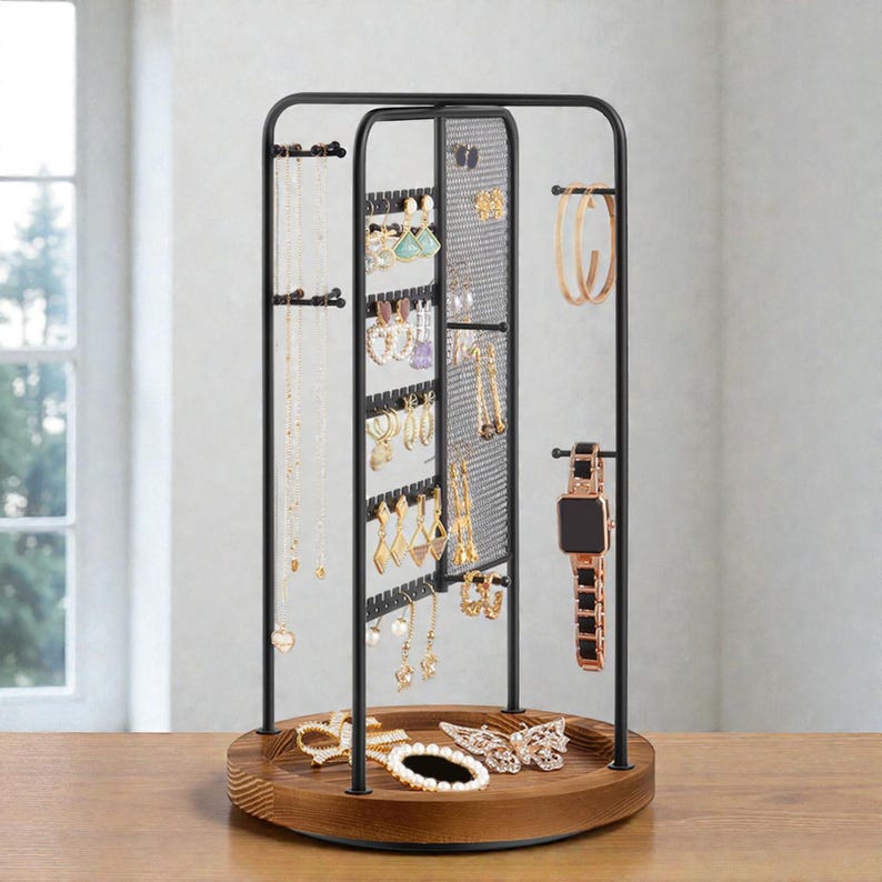 May include: A black metal jewelry organizer with a wooden base. The organizer features multiple levels for hanging necklaces, earrings, and bracelets. A watch and hoop earrings are also displayed. The jewelry stand is on a wooden table.